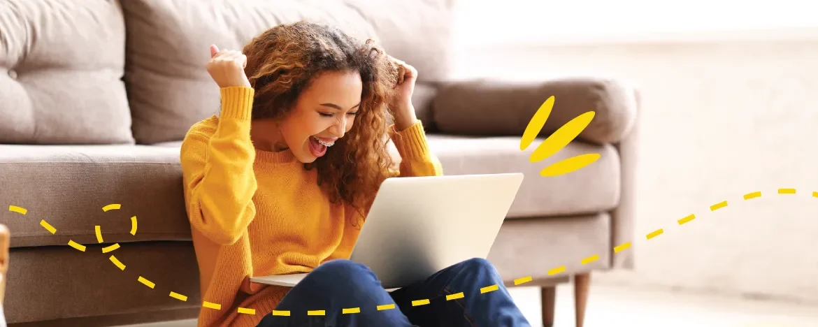 Woman with laptop on her lap, arms up in the air smiling