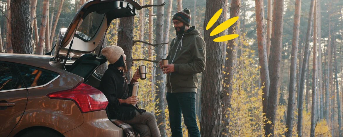 Person sat in back of their car drinking a warm drink and talking to a friend