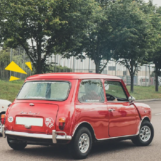 An old, red car in an abandoned city and surrounded by overgrown foliage