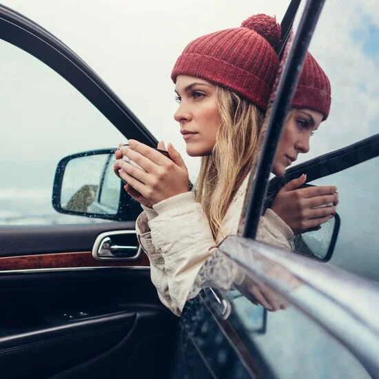 Person sat in front car seat with door open and holding a hot drink