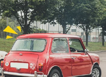 An old, red car in an abandoned city and surrounded by overgrown foliage